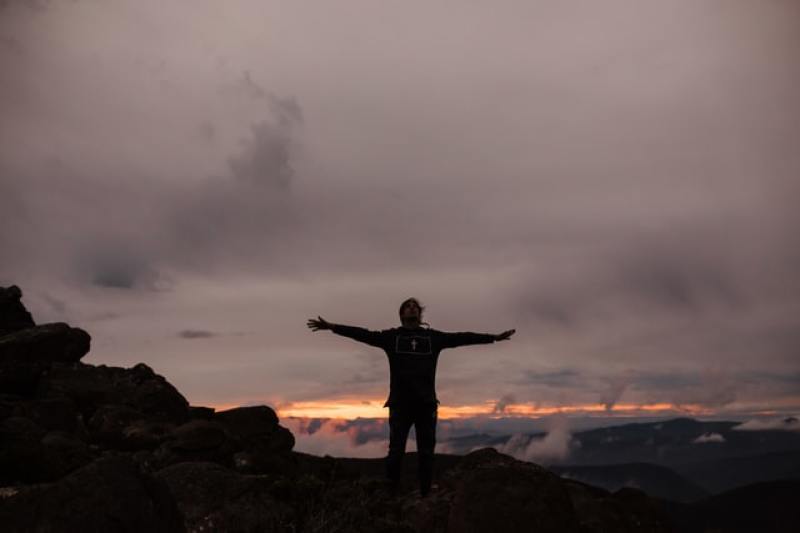 man raising hands worshiping God beneath a dark gloomy sky