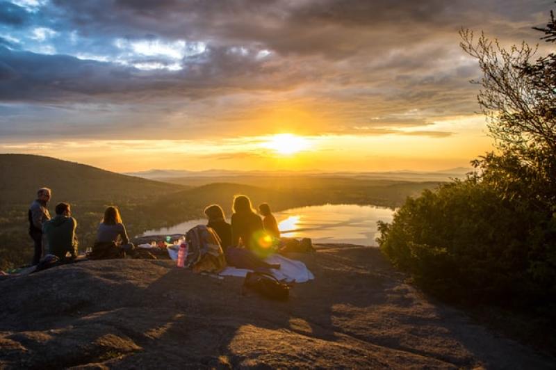 young people having a picnic while looking at the sunset